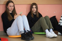 Dwie dziewczyny siedzą na podłodze oparte plecami o ścianę.