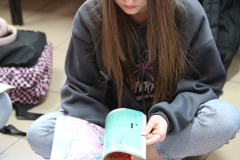 Siedząca na podłodze po turecku długowłosa dziewczyna kartkuje magazyn. Przed nią kartka z naklejonymi obrazkami.