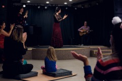 Publiczność klaszcze wraz z tancerką flamenco stojącą na scenie.