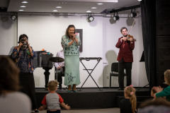 Muzycy na scenie. Od lewej: kobieta grająca na tamburynie, klaszcząca wokalistka i skrzypek.