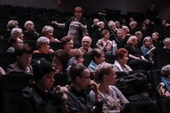 Publiczność siedząca w ciemnych fotelach sali widowiskowej.