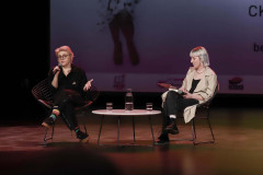 Na scenie w fotealch siedzą Maria Peszek i Marta Duszyńska. Między nimi stolik. W tle fragment slajdu z nogami.