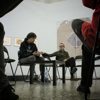 Zdjęcie z ptasiej perspektywy. Po bokach nogi uczestników spotkania. W środku kadru Piotr Tkacz i Robert Brzęcki przy stoliku.