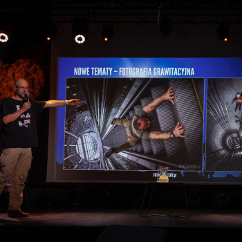 Tomasz Kulas stoi na scenie i wskazuje na slajd z napisem Nowy temat - fotografia grawitacyjna. Na zdjęciach człowiek na ruchomych schodach oraz robotnicy w tunelu.