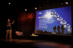 Tomasz Kulas stoi na scenie i wskazuje slajd ze zdjęciem, napisami z punktem 1. MISJA.