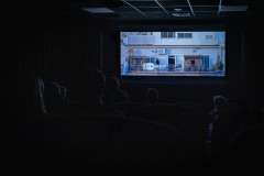 Ciemność sali kinowej, zarysy głów i kadr z filmu wyświetlony na ekranie.