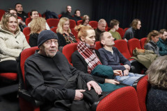 Zdjęcie grupowe. Widzowie siedzący w czerwonych fotelach kinowych. Na pierwszym planie Włodek Sypniewski w czapce na głowie patrzy w obiektyw.