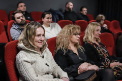 Zdjęcie widzów siedzących w czerwonych fotelach kinowych. Zbliżenie na trzy kobiety.