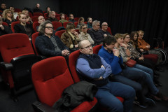 Zdjęcie grupowe. Widzowie zasiadający w czerwonych fotelach kinowych. W głębi kadru ciemna kotara.
