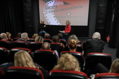 Zdjęcie zrobione zza rzędów foteli. Głowy widzów, a w głębi kadru siedzący na krzesłach Grzegorz Paprzycki i Paulina Pachulska-Wojdak. Za nimi wyświelony slajd Środy z kinem niezależnym.