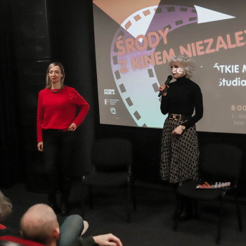 Przed ekranem stoją (po lewej): Karolina Porcari i Paulina Pachulska-Wojdak z mikrofonem ( po prawej). Za nimi wyświetlony slajd Środy z kinem niezależnym.