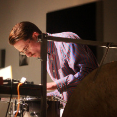 Zbliżenie na mężczyznę pochylonego nad instrumetami. Ubrany w koszulę w paski. Sfotografowany z lewego profilu. 