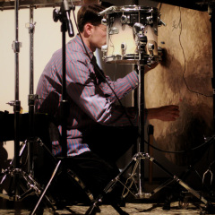 Mężczyzna kucający przy instrumentach perkusyjnych. 