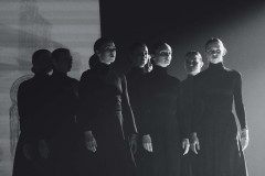 Grupa stojących obok siebie tancerek w długich sukienkach. Czarno-białe zdjęcie w planie amerykańskim.