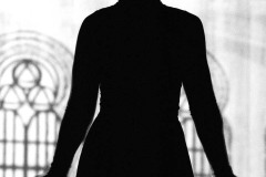 Zarys ciemnej kobiecej sylwetki na jasnym slajdzie ze szkicem okien synagogi. Zdjęcie czarno-białe.