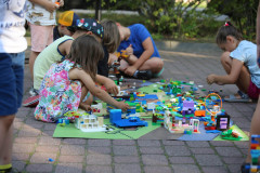 Na chodniku rozłożona plansza z klockami Lego. Wokół niej kucają dzieci.