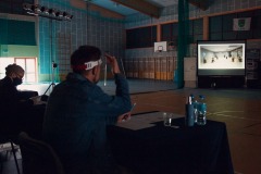 Członkowie komisji siedzą tyłem przy stolikach. Oglądają nagranie wyświetlane na projektorze.