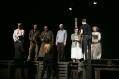 Aktorzy spektaklu Kyś stoją rzędem na scenie. Pantomimiści wręczają im czerwone róże.