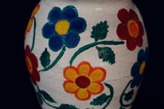 Biały wazon z czerwoną obwódką u szczytu. Ozdobiony kwiatami w kolorach żółtym, niebieskim i czerwonym.