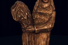 Drewniana figurka przysadzistej kobiety trzymającej zboże.