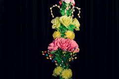 Podłużny bukiet różnokolorowych kwiatów wykonanych z bibuły. Włożony w dzbanek ozdobiony motywem żonkili.