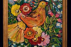 Niewielkich rozmiarów obraz oprawiony drewnianą ramką. Przedstawia pomarańczowo-żółtego ptaka pośród różnego koloru kwiatów.
