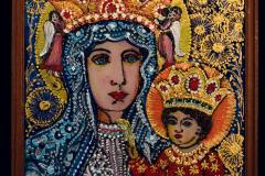 Obraz przedstawiający Matkę Boską z Dzieciątkiem. Po bokach głowy kobiety znajdują się małe postaci aniołów.  Granatowe tło ozdobione jest złotymi kwiatami.  Obraz oprawiono drewnianą ramą.