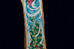 Malowidło na przekroju pieńka przedstawia Matkę Boską z Dzieciątkiem otulonych Jej niebieskimi skrzydłami. Zieloną spódnicę zdobią stokrotki. Wokół głowy ma żółto-czerwoną aureolę.