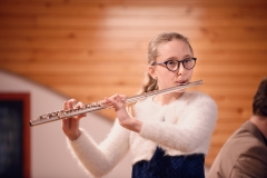 Dziewczynka w okulrach i białym sweterku gra na flecie.
