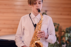 Chłopiec w białej koszuli gra na saksofonie.