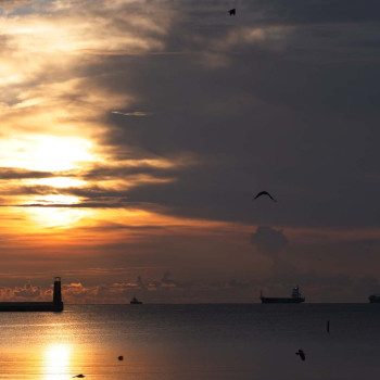 Zachód słońca nad morzem. Statki wpływające do portu.