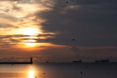 Zachód słońca nad morzem. Statki wpływające do portu.