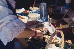 Kobieta smaruje smalcem pajdę chleba. Na stole chleb w koszyku i inne naczynia.