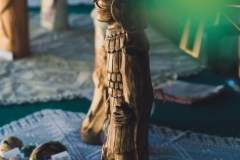 Zbliżenie na drewnianą rzeźbę ludową ustawioną na szydełkowej serwecie. Obok leżą pisanki.