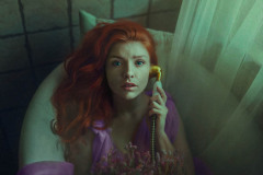 Kobieta w liliowej sukience leży w wannie ze słuchawką starego telefonu. Patrzy w obiektyw. Po prawej zwoje tiulu.