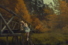Kobieta siedzi na drewnianym moście. W tle jesienne drzewa.
