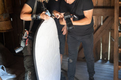 Kobieta trzymająca blendę i dwóch mężczyzn oglądają zdjęcia na wyświetlaczu aparatu fotograficznego.