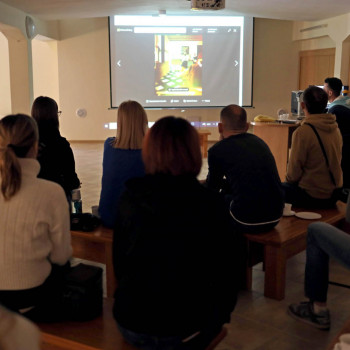 Grupa osób siedzących tyłem do obiektywu. Przed nimi slajd wyświetlony na ściennym ekranie.
