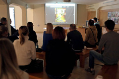 Grupa osób siedzących tyłem do obiektywu. Przed nimi slajd wyświetlony na ściennym ekranie.