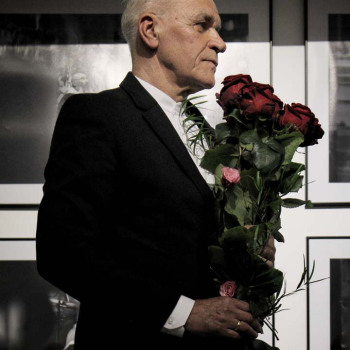 Sfotografowany z prawego profilu Franciszek Kupczyk w ciemnym garniturze i z bukietem długich czerwonych róż. Zdjęcie w planie amerykańskim.