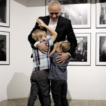 Franciszek Kupczyk przytula dwoje dzieci. Za nimi fotografie wyeksponowane na ścianie.