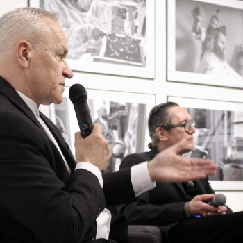 Sfotografowany z prawego profilu Franciszek Kupczyk. Siedzi w fotelu i mówi do mikrofonu trzymanego w prawej dłoni. W głębi Robert Brzęcki w fotelu i cztery fotografie na ścianie.