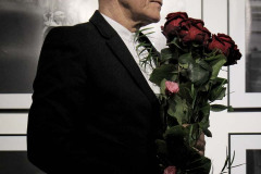 Sfotografowany z prawego profilu Franciszek Kupczyk w ciemnym garniturze i z bukietem długich czerwonych róż. Zdjęcie w planie amerykańskim.