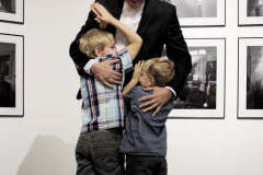 Franciszek Kupczyk przytula dwoje dzieci. Za nimi fotografie wyeksponowane na ścianie.