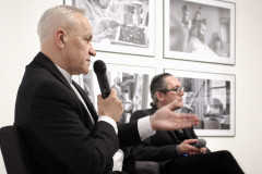 Sfotografowany z prawego profilu Franciszek Kupczyk. Siedzi w fotelu i mówi do mikrofonu trzymanego w prawej dłoni. W głębi Robert Brzęcki w fotelu i cztery fotografie na ścianie.