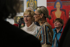 Krystyna Ruminkiewicz pośród gości. Po lewej ciemny bark mężczyzny. Na ścianie prace - portrety kobiet.