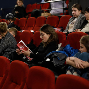 Uczestnicy konkursu w czerwonych fotelach. W centrum kadru dziewczyna z folderem Młodzi Koryfeusze.