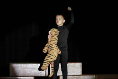 Chłopiec w czernym stroju z pluszakiem tygrysem. Unosi w górę lewą rękę.