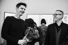 Artysta fotograf Wojciech Moskwa trzyma bukiet kwiatów. Obok stoi uśmiechnięty Robert Brzęcki.