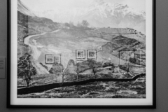 Fotografia oprawiona czarną ramą. Przedstawia góry. W szkle odbija się wnętrze Galerii Wieża Cieśnień.